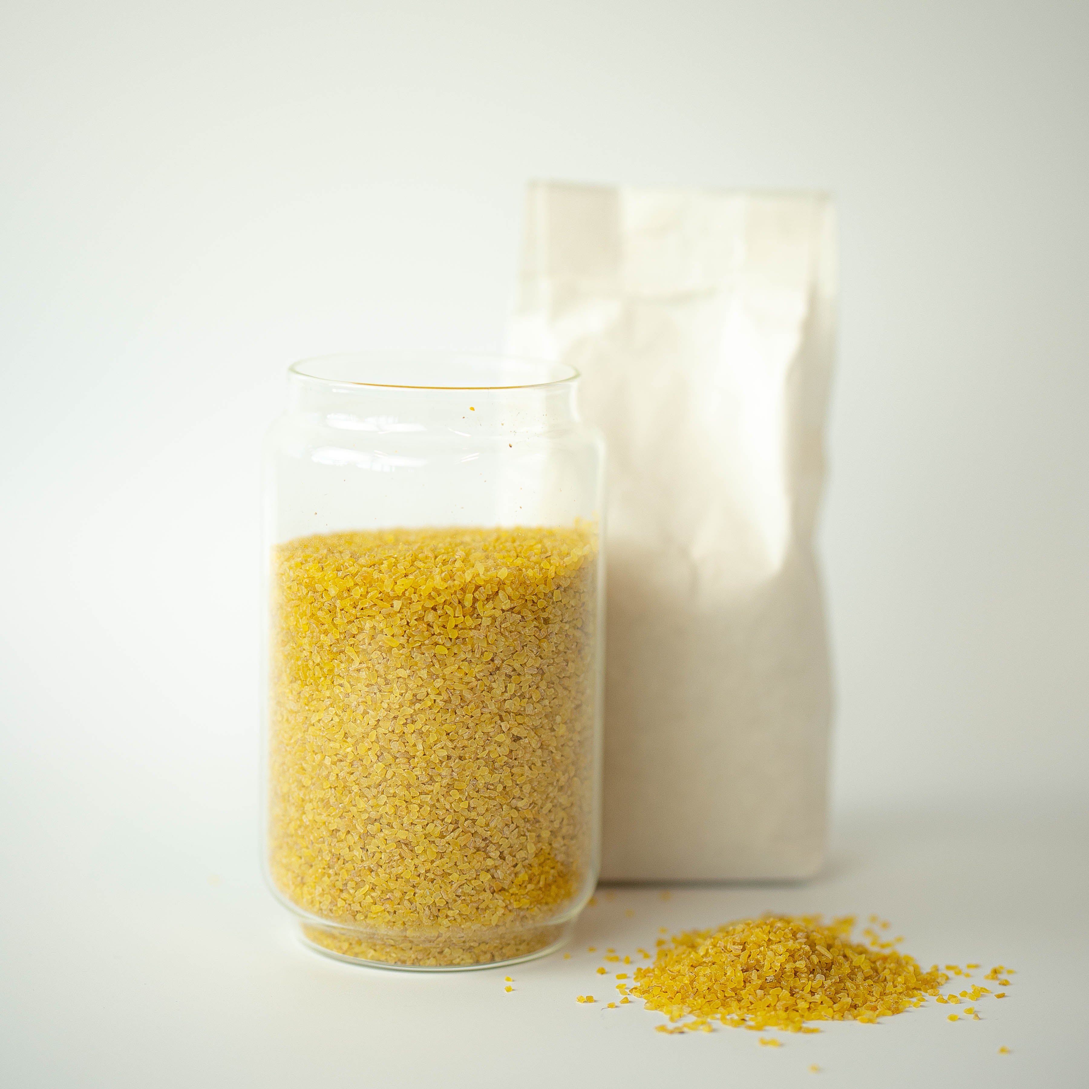 A glass jar filled with organic bulgur wheat, with a recyclable paper bag in the background and a small pile of bulgur wheat in the foreground.
