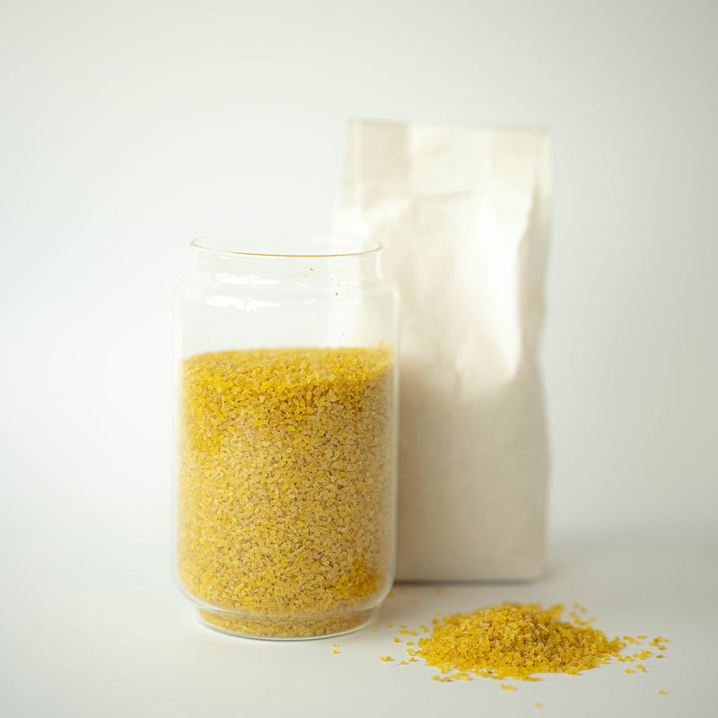 A glass jar filled with organic bulgur wheat, with a recyclable paper bag in the background and a small pile of bulgur wheat in the foreground.