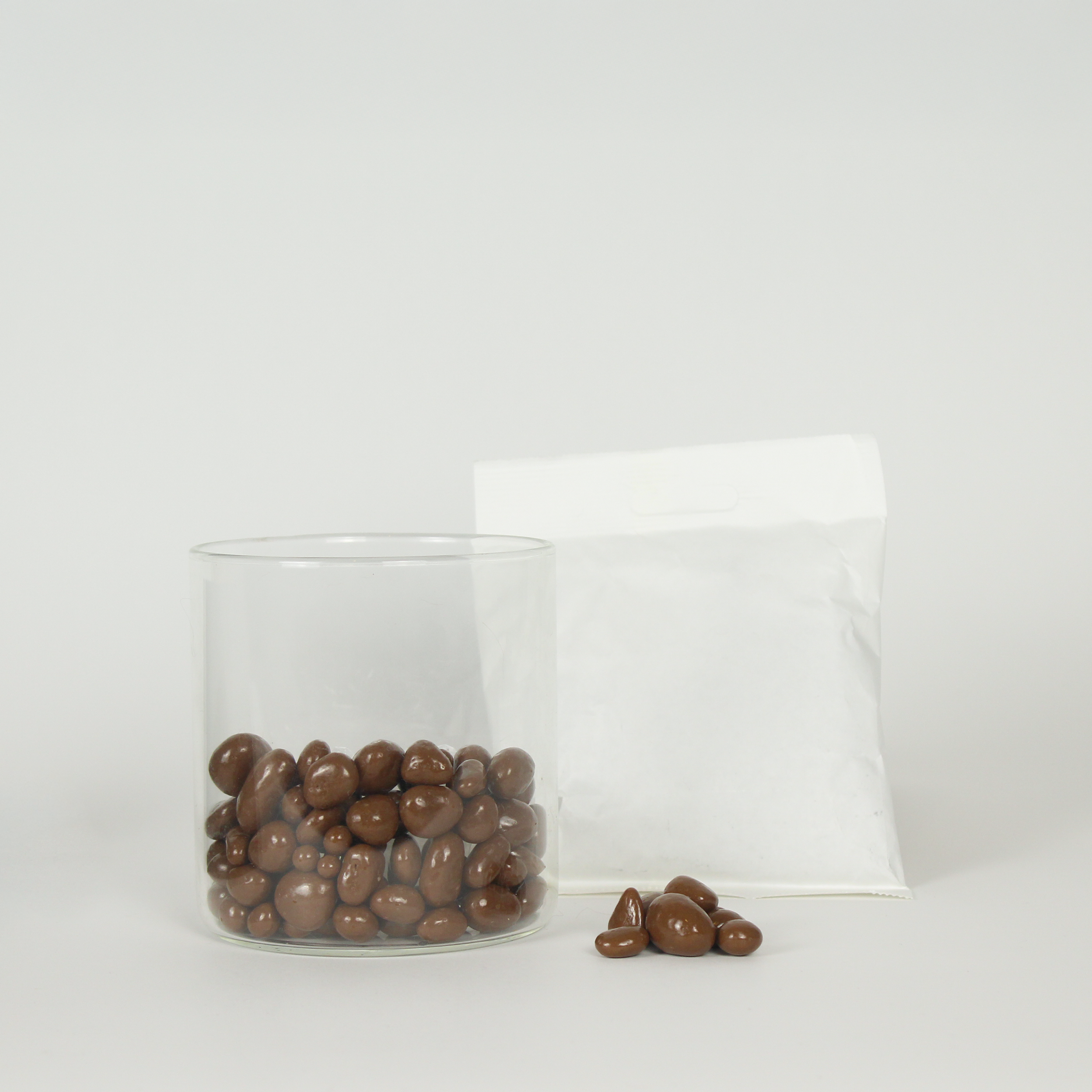 Glass container and white bag filled with chocolate-covered honeycomb on a white background