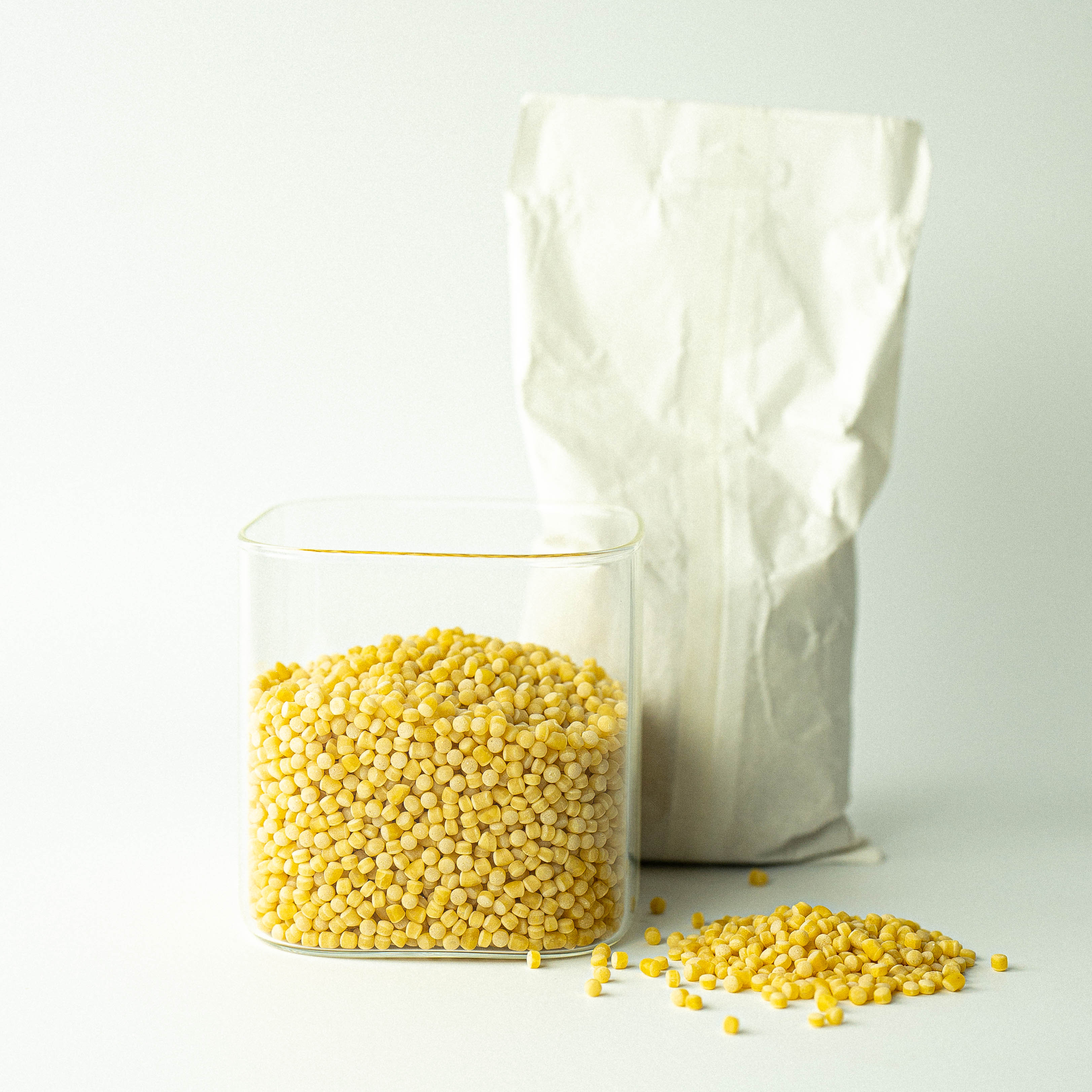 A glass jar filled with yellow couscous grains next to a recyclable paper bag, with some grains scattered in front.
