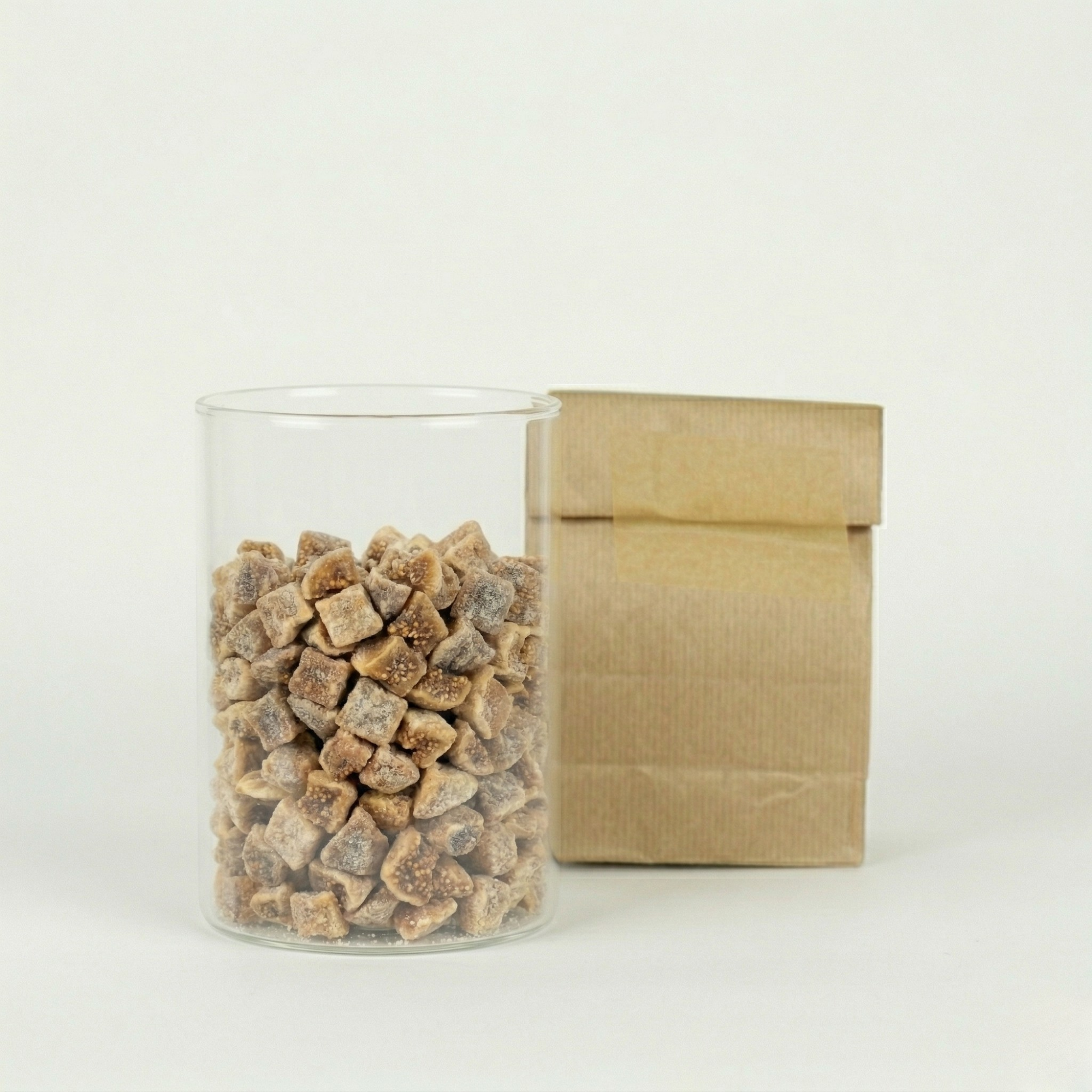 Clear glass jar filled with chopped figs next to a brown paper bag on a white background