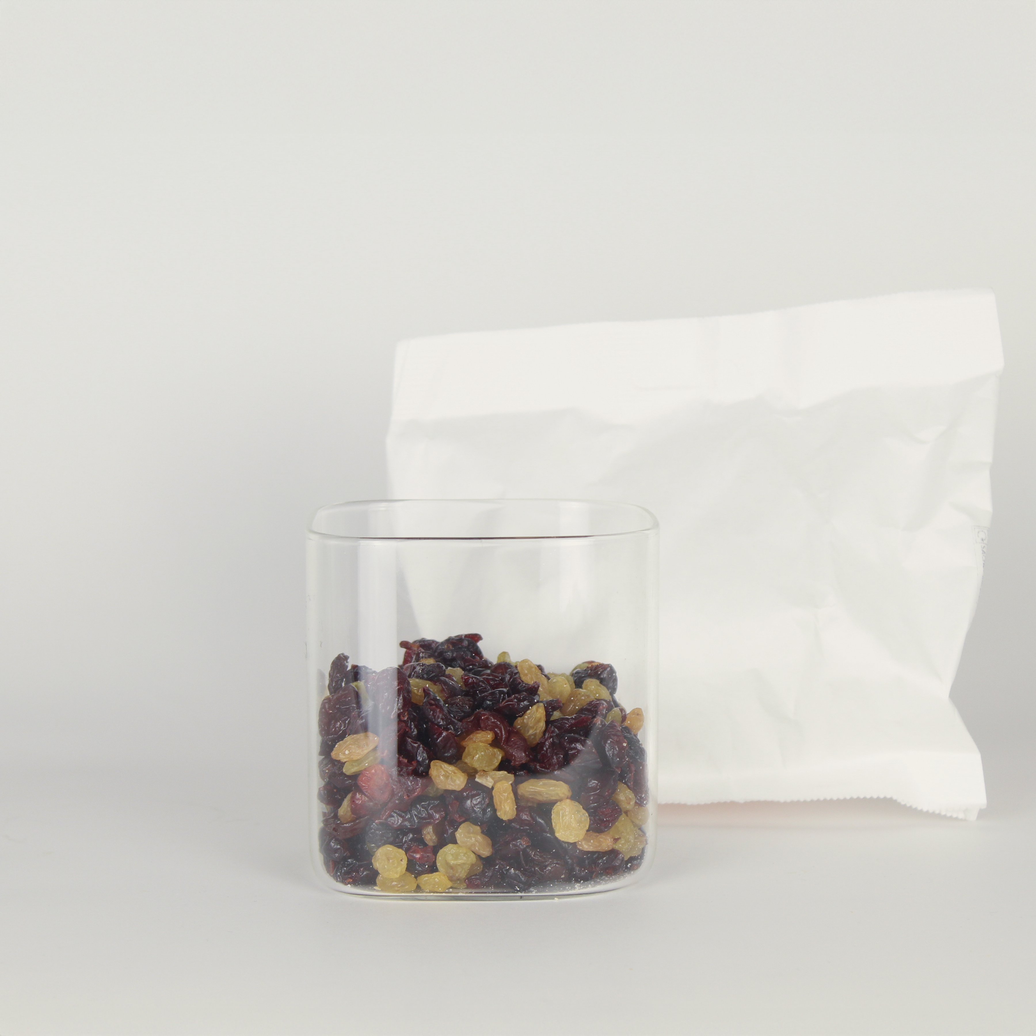Clear glass jar with dried fruits and a white fabric bag on a light gray background