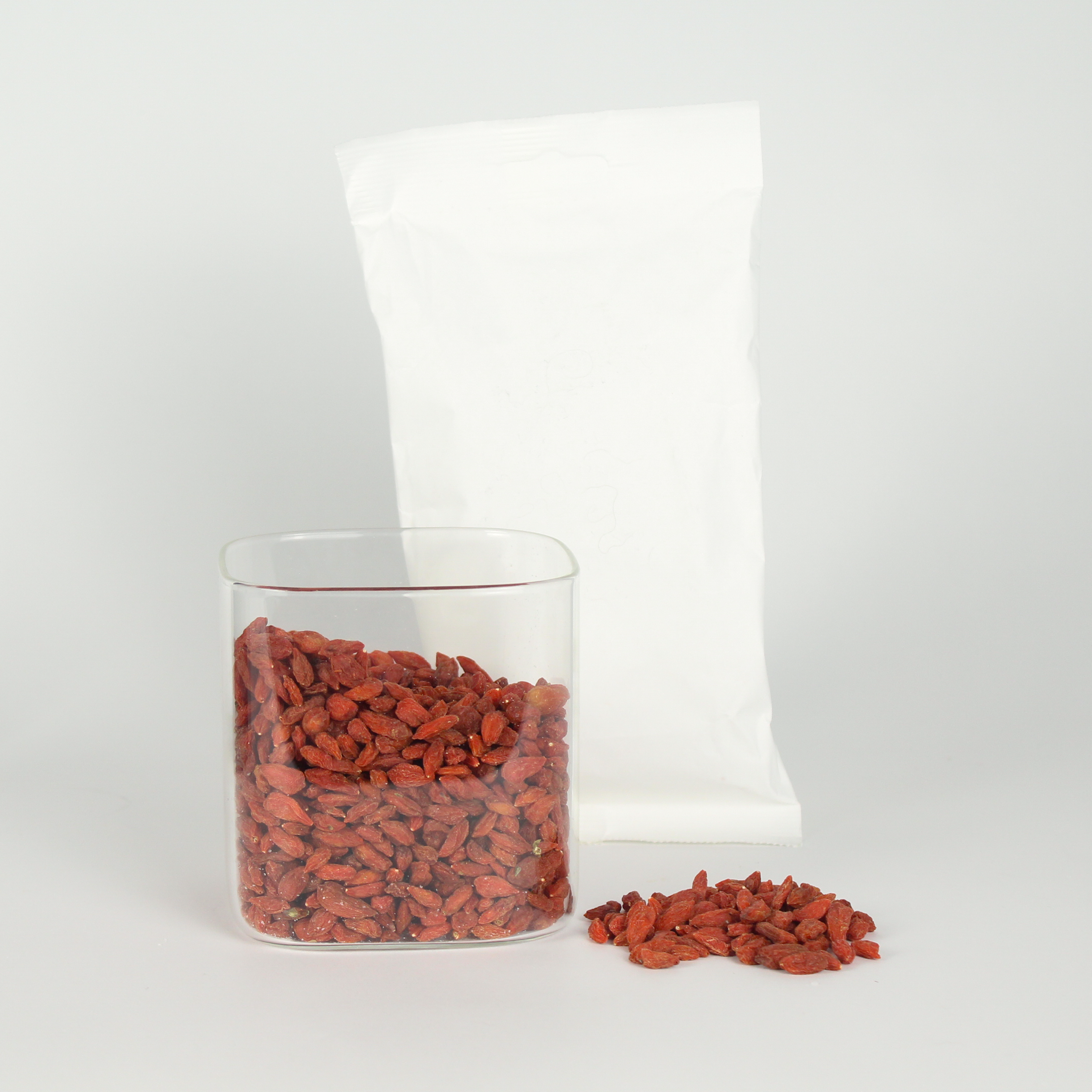 Red goji berries in a clear container with a white bag on a light gray background