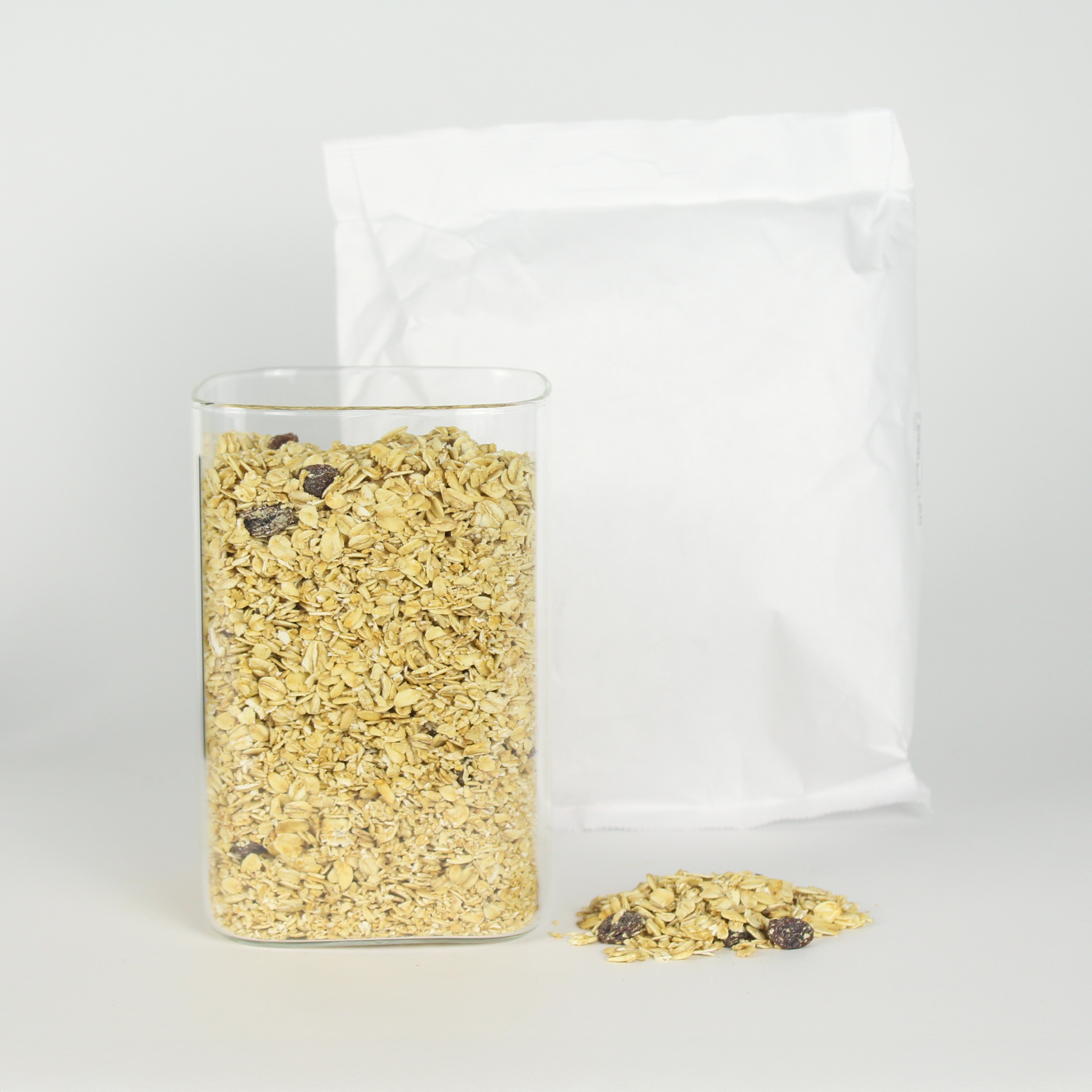 Glass jar of granola with a white bag on a light gray background