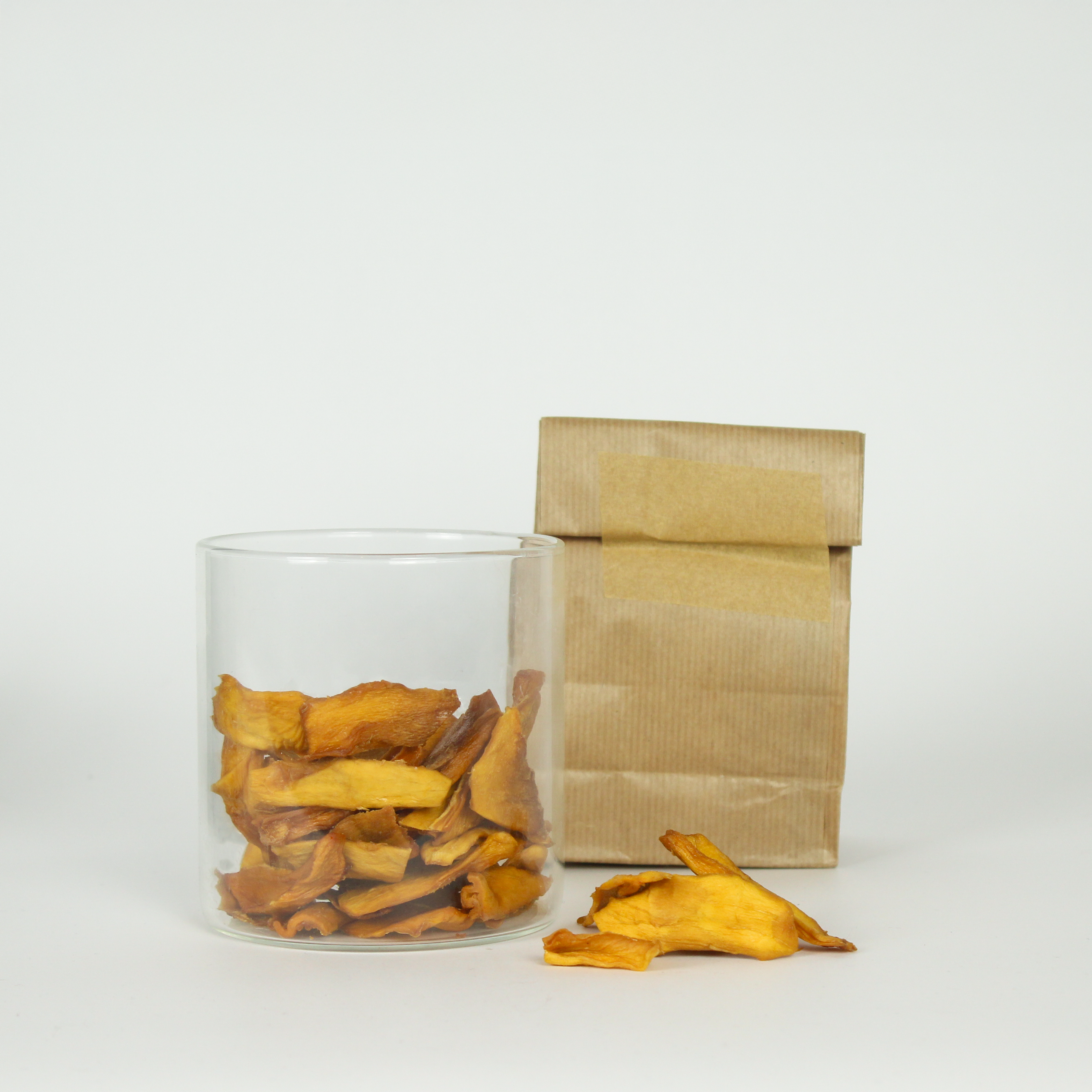 Clear glass jar with sliced mango, brown paper bag on a white background