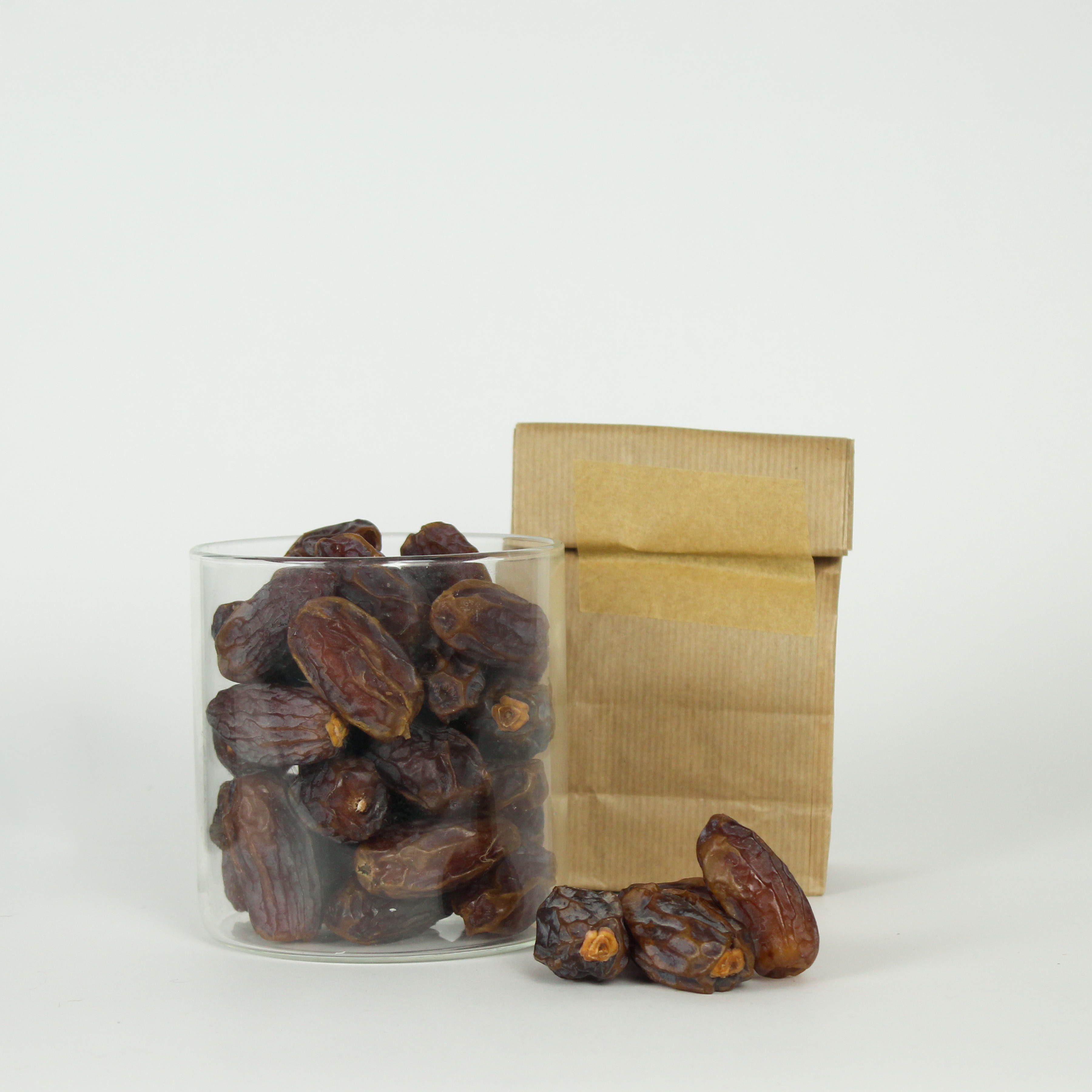 Glass jar filled with dates and a brown paper bag on a white background