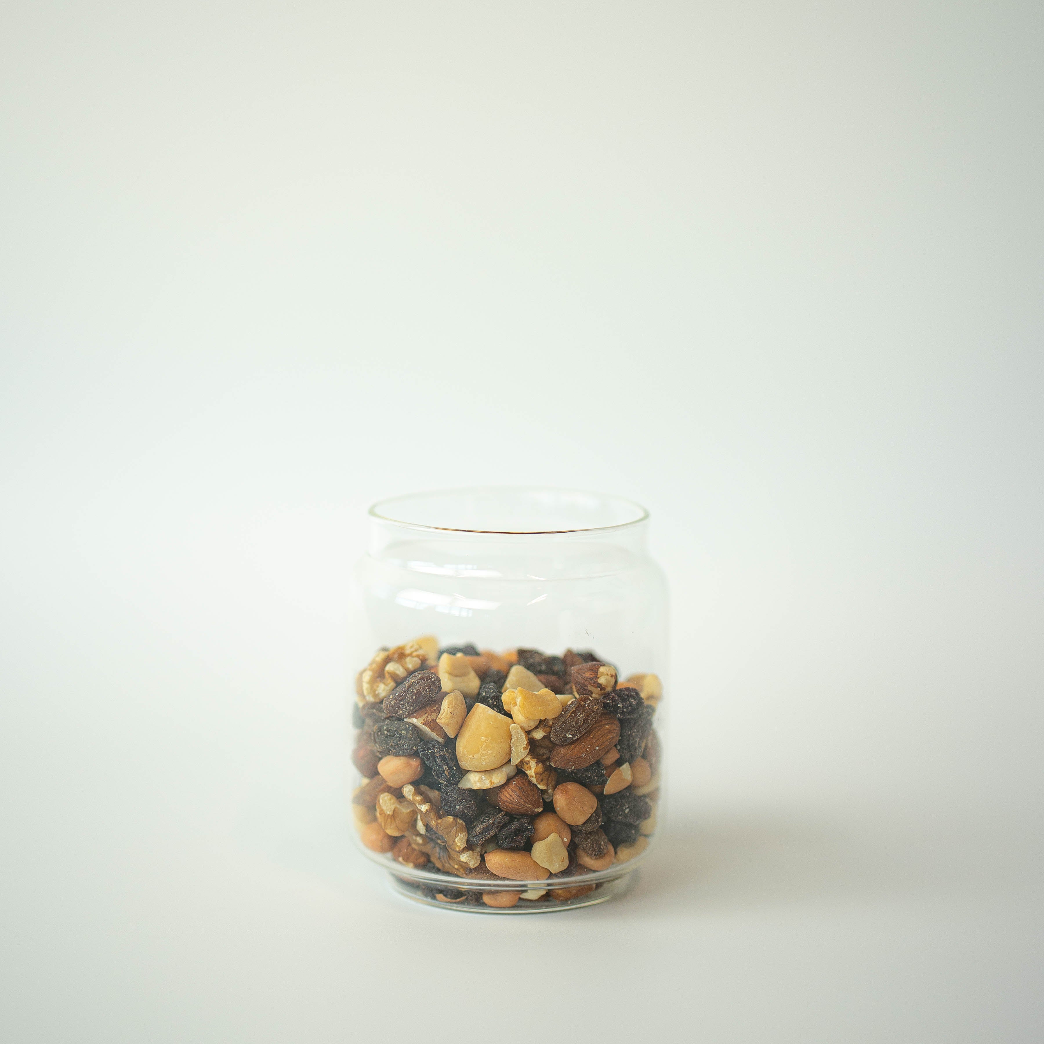 A clear glass jar filled with a mix of dried fruits and nuts on a white background.