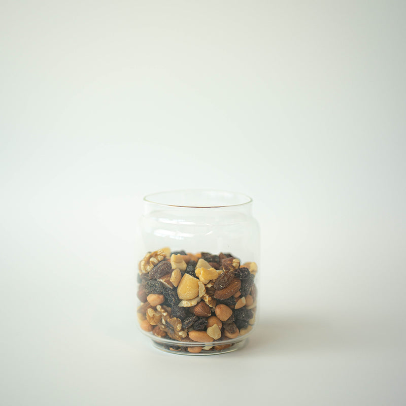 A clear glass jar filled with a mix of dried fruits and nuts on a white background.