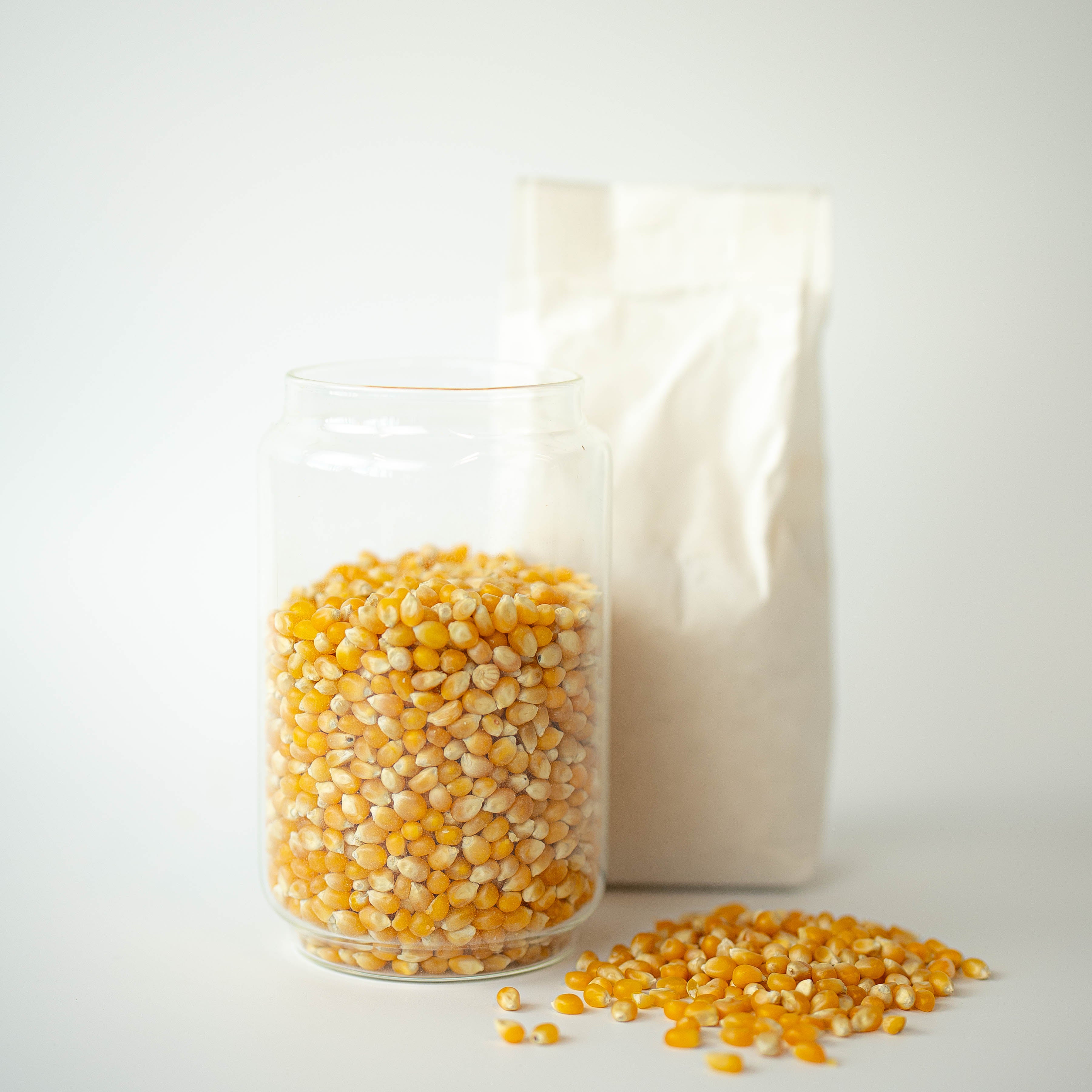 Popping corn in a jar, with a bag behind and a pile next to it.