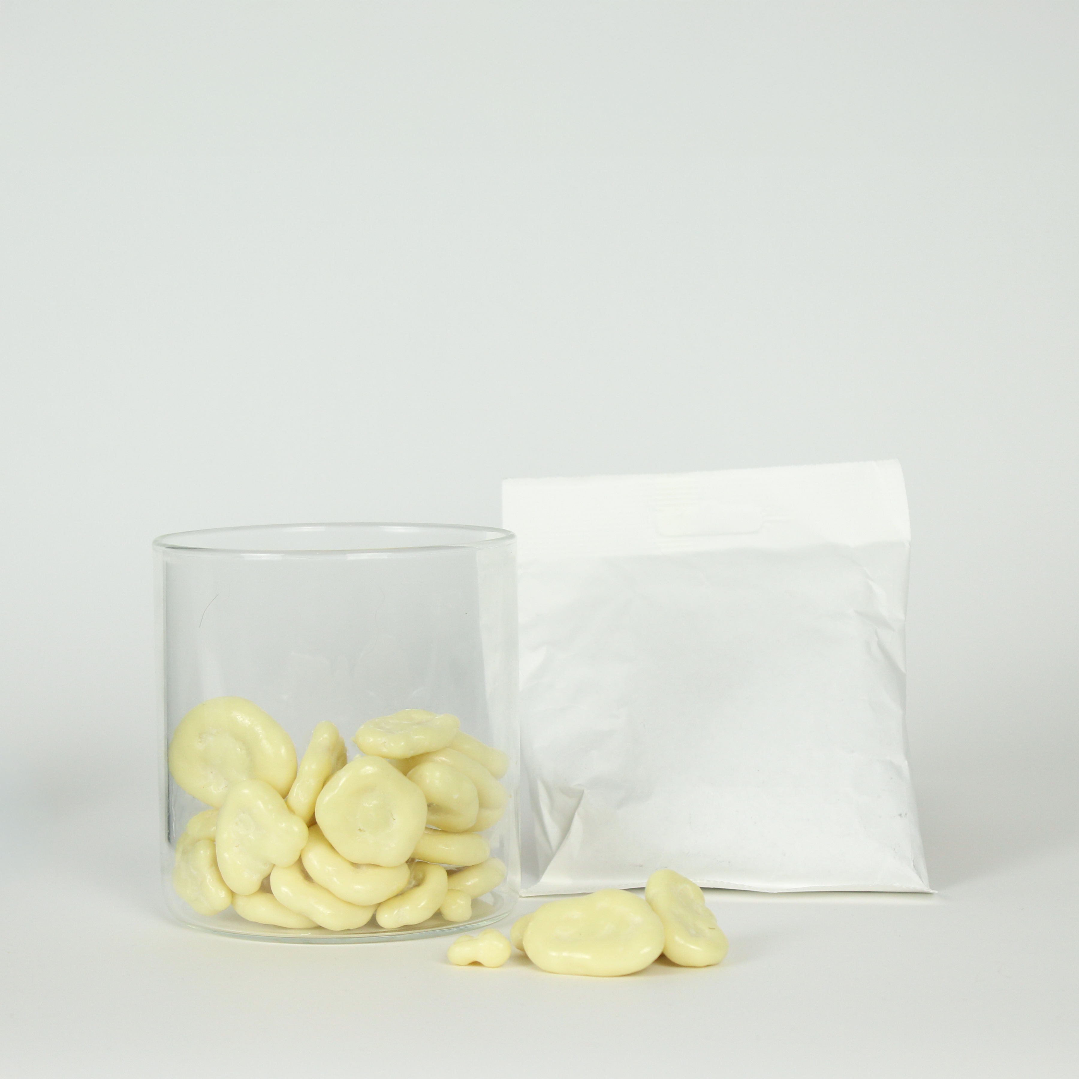 Clear glass container with yoghurt covered banana chips on a light gray background